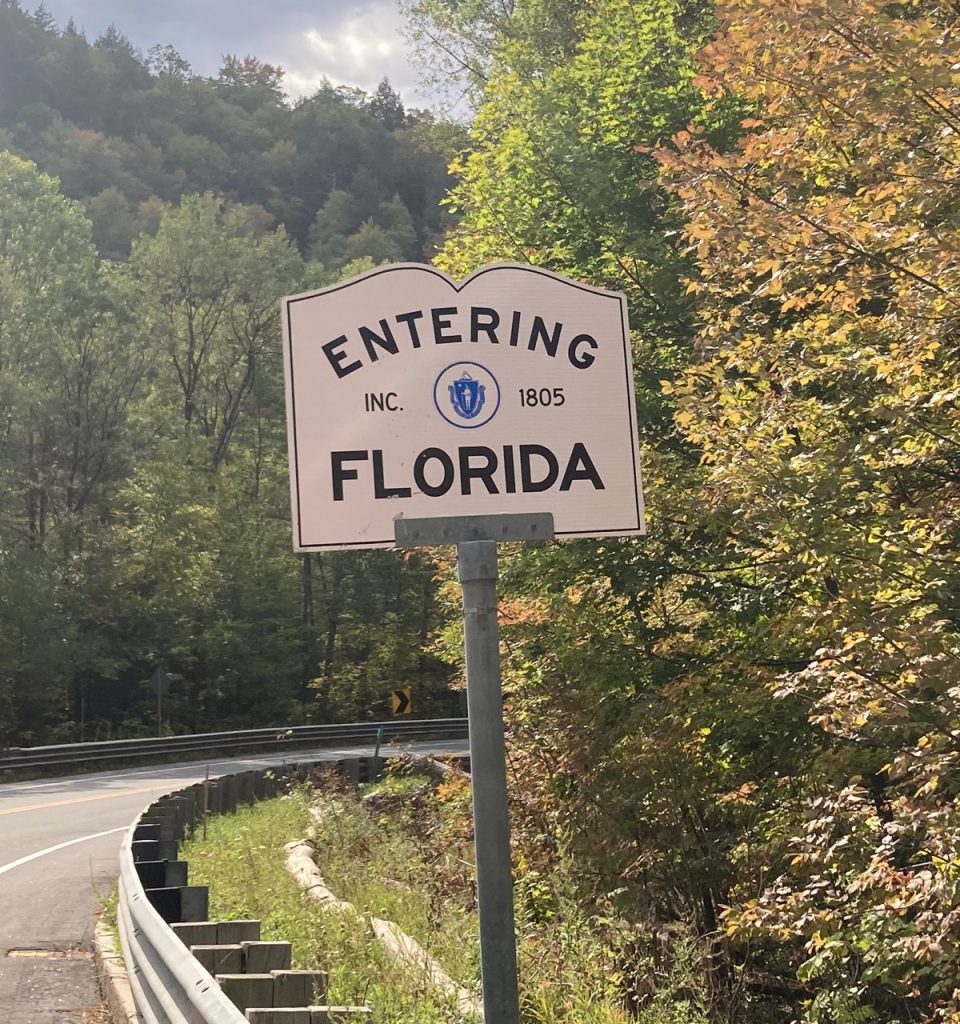 White sign by the side of the road, with black lettering reading "Entering Florida".  There are a lot of trees around.