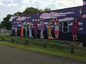 Mural on the side of a building, depicting nine women of different ages, races, and ethnicities, each holding a burning torch aloft in one hand.