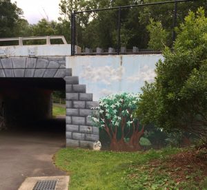 Mural of a flowering bush as well as painted stones on the concrete wall of a bike tunnel entrance.