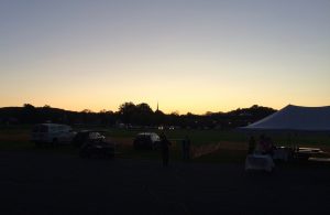 Sunrise in background, with cars and the edge of a canopy in front of a field.