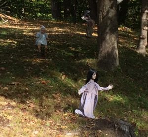 Close view of 2 creepy dolls on lawn, in the shadow of some trees.