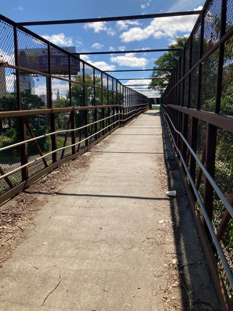 Looking along bike and pedestrian bridge with a concrete deck and metal frame with chainlink walls