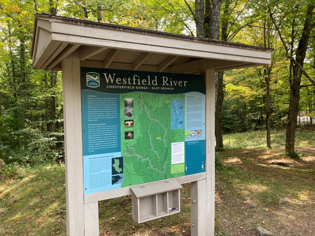 Large signboard with signs about the Chesterfield Gorge on the Westfield River, East Branch.  Woods can be seen behind the board.