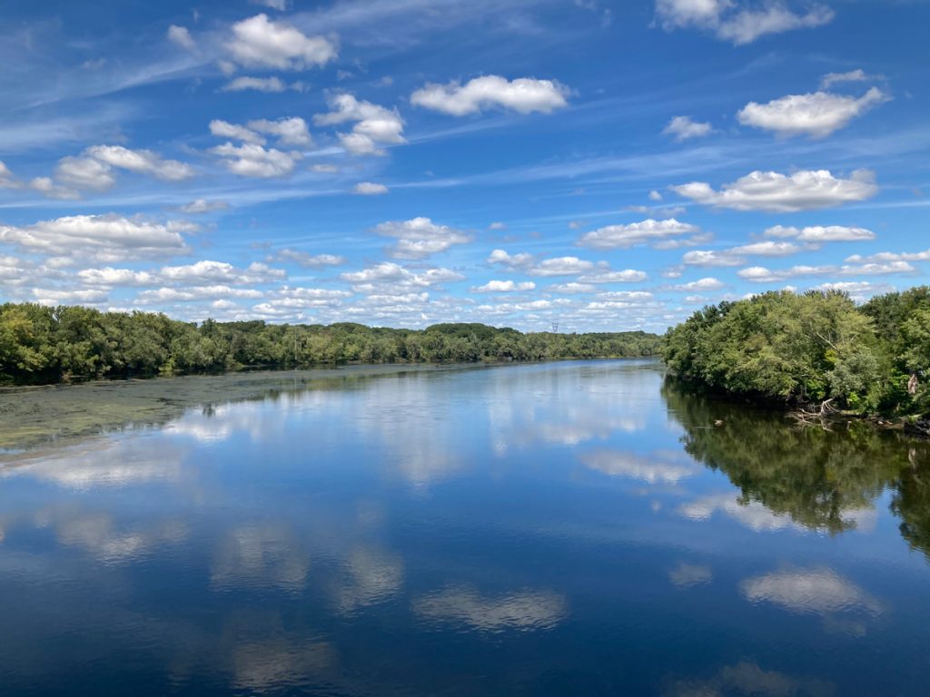 View of river with trees on either side, and reflections of clouds in water.