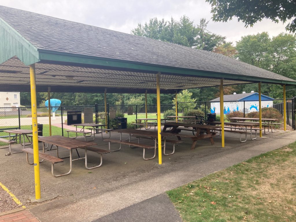Picnic shelter with yellow supporting columns and several picnic tables.