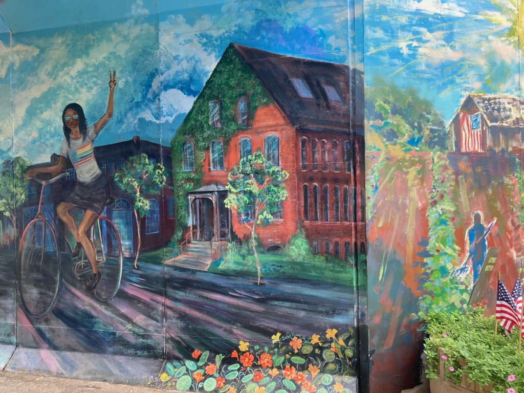 Mural panel depicting waving cyclist and a house covered in ivy