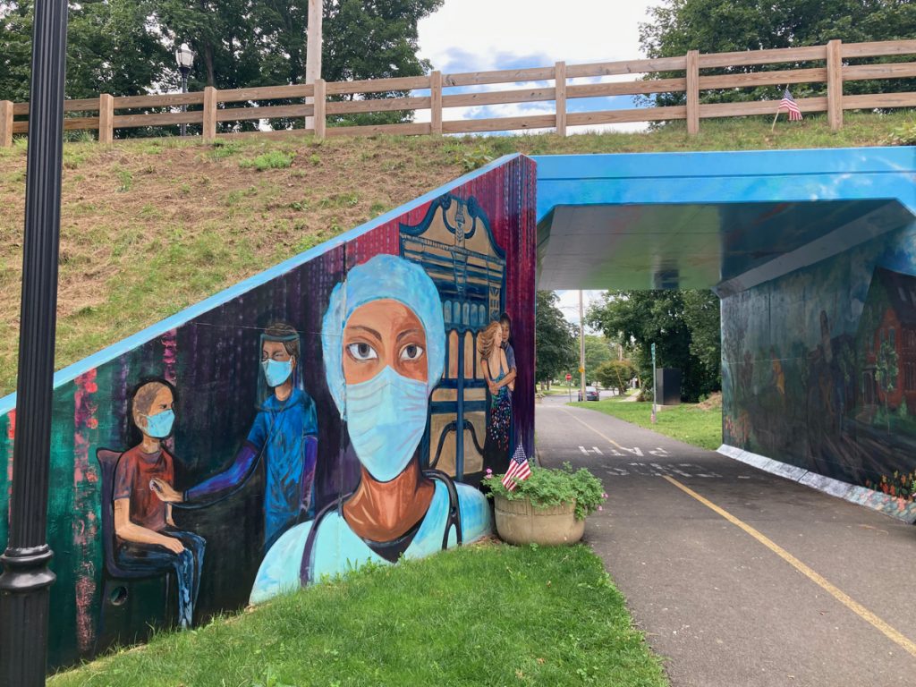 Tunnel under bike path, with a mural to the left of the entrance, depicting health care workers wearing masks