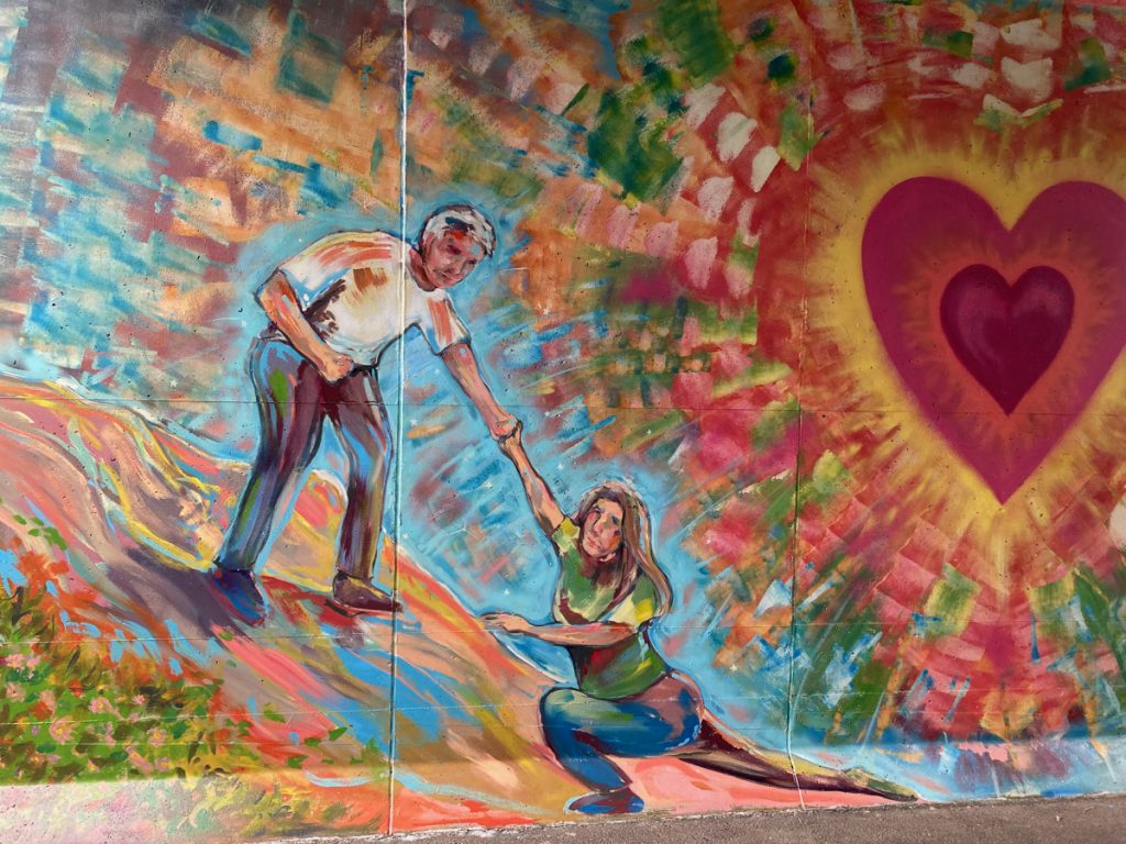 Mural depicting one person helping another up, next to a lage red heart that is glowing and radiating color