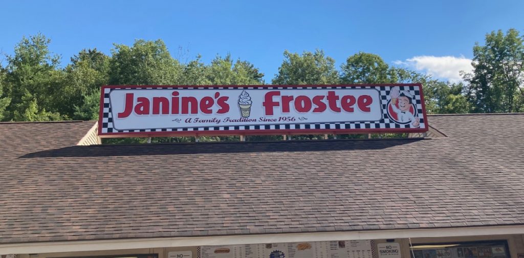 Sign on a roof of building, which reads "Janine's Frostee", with a picture of a soft-serve cone.