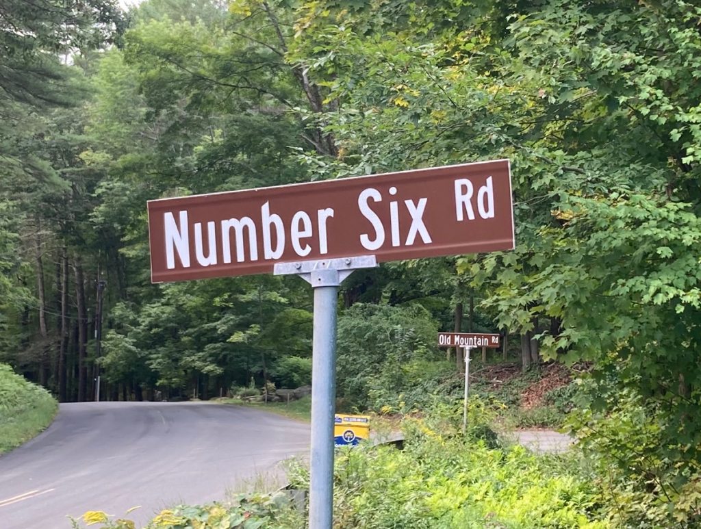 Street sign reading "Number Six Road", with trees in background