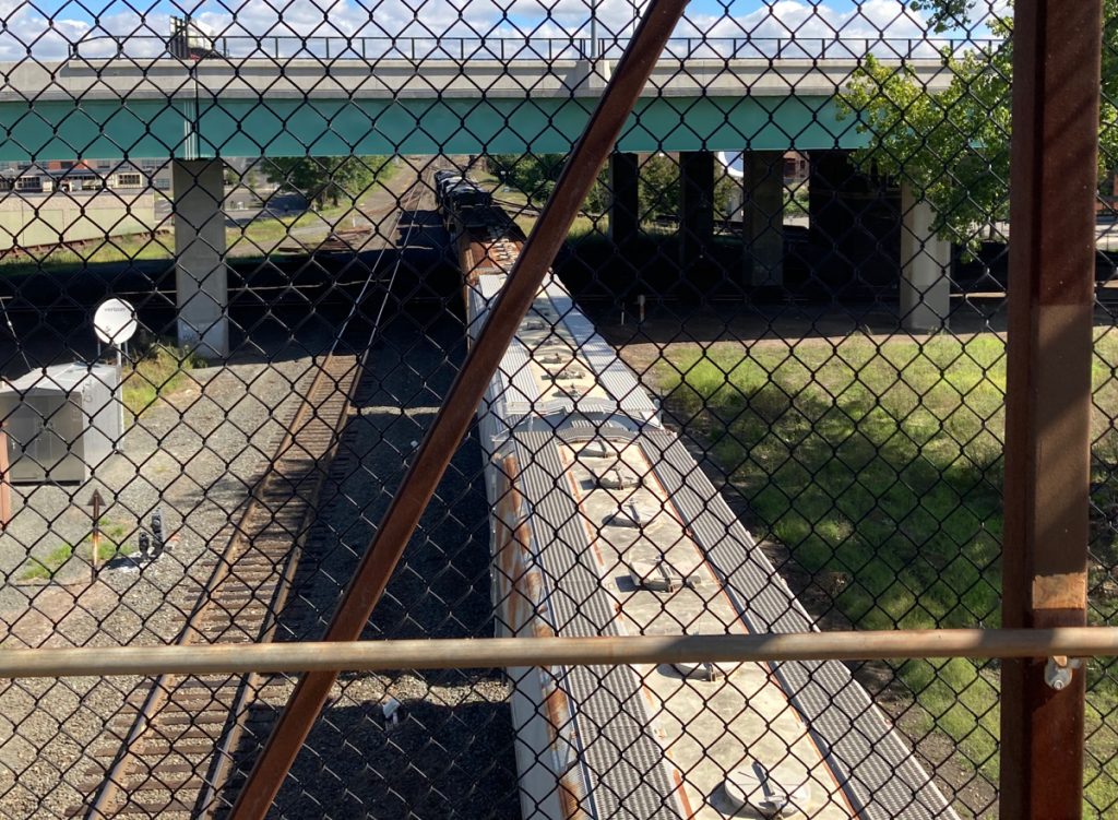 Looking down through chainlink fence at a train heading away from the camera