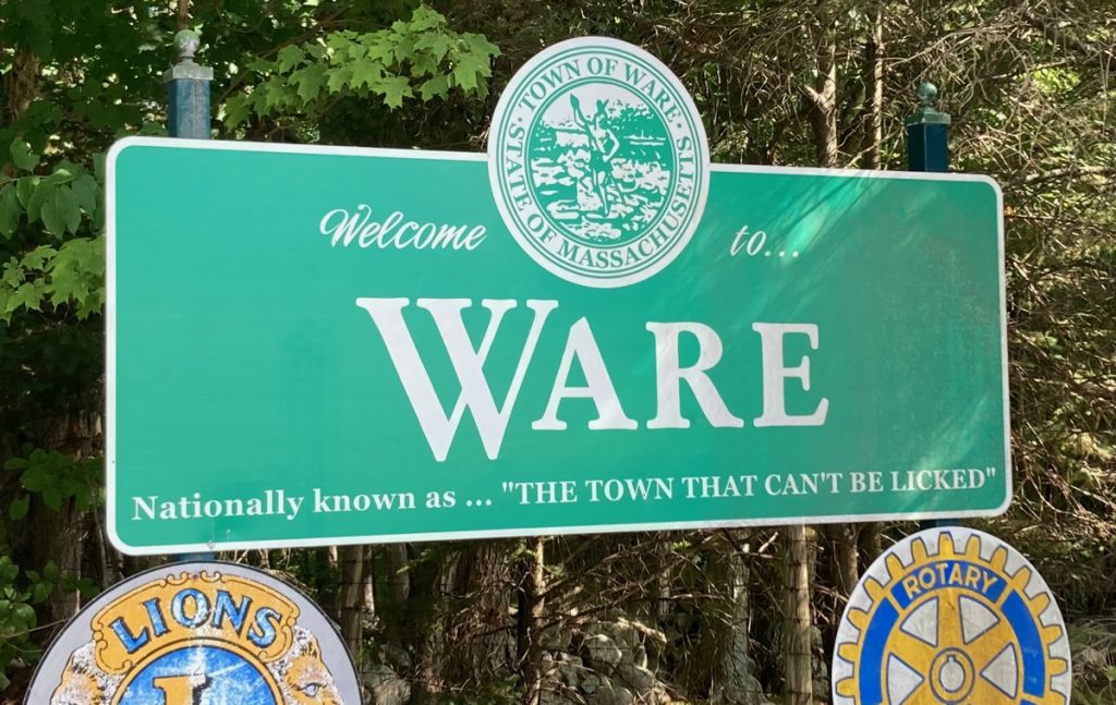 Large green roadside sign reading "Welcome to Ware.  Nationally known as the town that can't be licked."