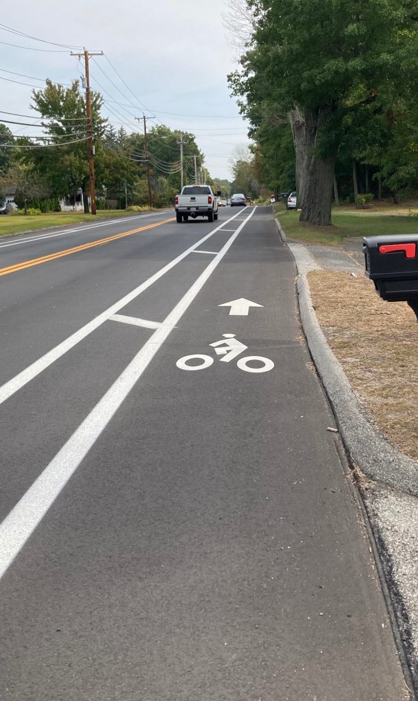 Road surface with bike lane painted on it, stretching off into distance, with some trees on the side of the road a ways away.