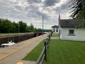 Looking along edge of lock - the lock itself is to the left, with top of boat visible inside.  Two buildings are on the right side, with grass in foreground.